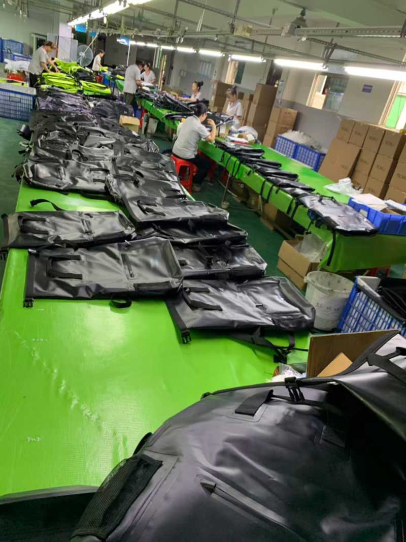 Long finishing line with welded black roll-top backpacks laid out on work tables